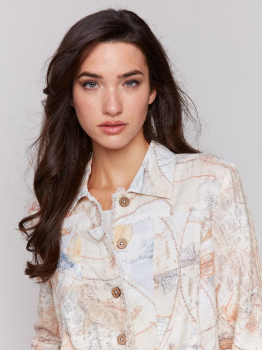 A person stands effortlessly against a plain background, wearing the Charlie B Frayed Linen Jacket and matching pants with a vintage map pattern. The ensemble creates a statement look featuring functional pockets that enhance its unique charm.