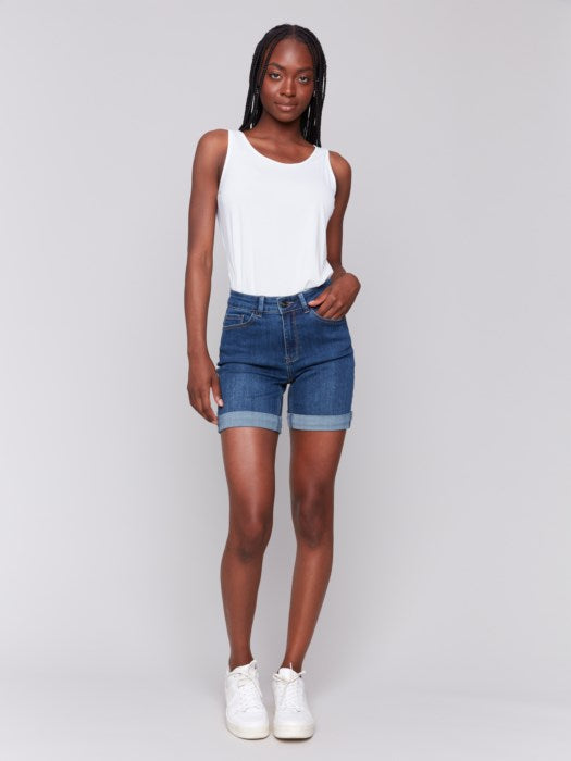 A person in Charlie B Rolled Cuff Denim Shorts and white sneakers stands sideways against a plain background, ideal for a casual summer occasion.