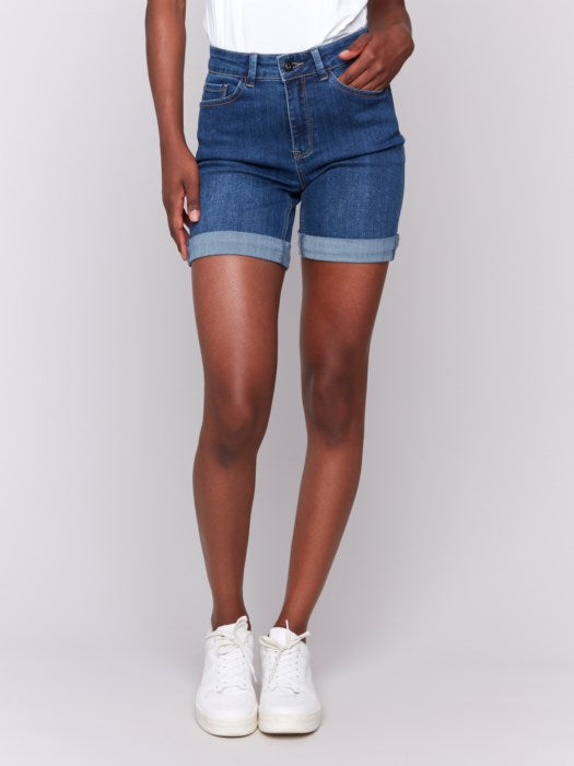 A person in Charlie B Rolled Cuff Denim Shorts and white sneakers stands sideways against a plain background, ideal for a casual summer occasion.