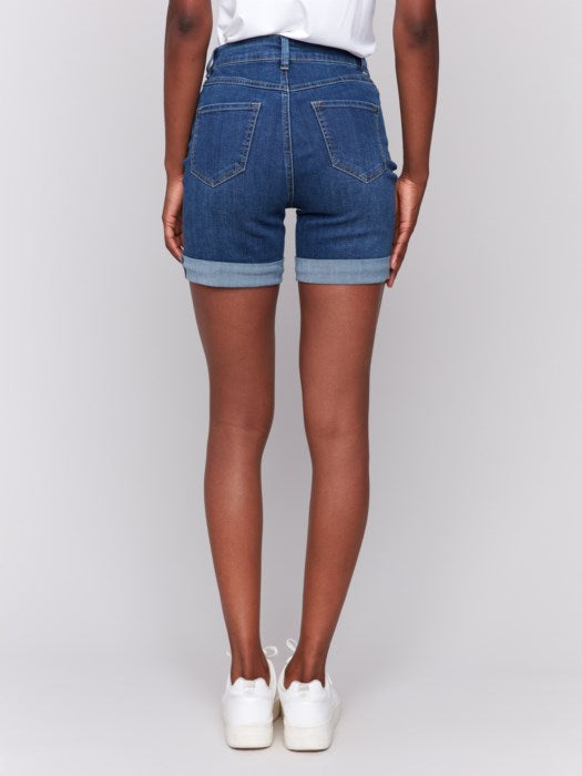 A person in Charlie B Rolled Cuff Denim Shorts and white sneakers stands sideways against a plain background, ideal for a casual summer occasion.