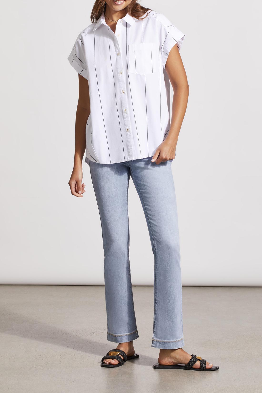 Woman wearing a Tribal striped cap sleeve shirt with cut details and jeans standing against a neutral background.