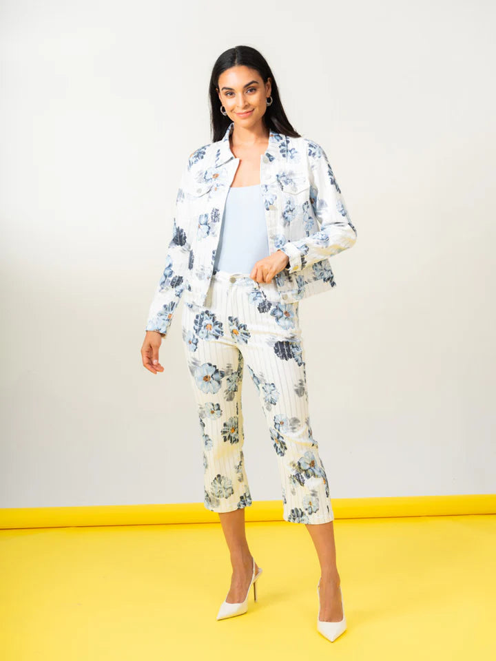 A woman confidently stands on a yellow floor against a white backdrop, showcasing her ensemble: an Elena Wang Floral Jacket paired with cropped pants—a stylish addition to any wardrobe.