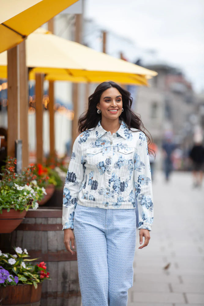 A woman confidently stands on a yellow floor against a white backdrop, showcasing her ensemble: an Elena Wang Floral Jacket paired with cropped pants—a stylish addition to any wardrobe.