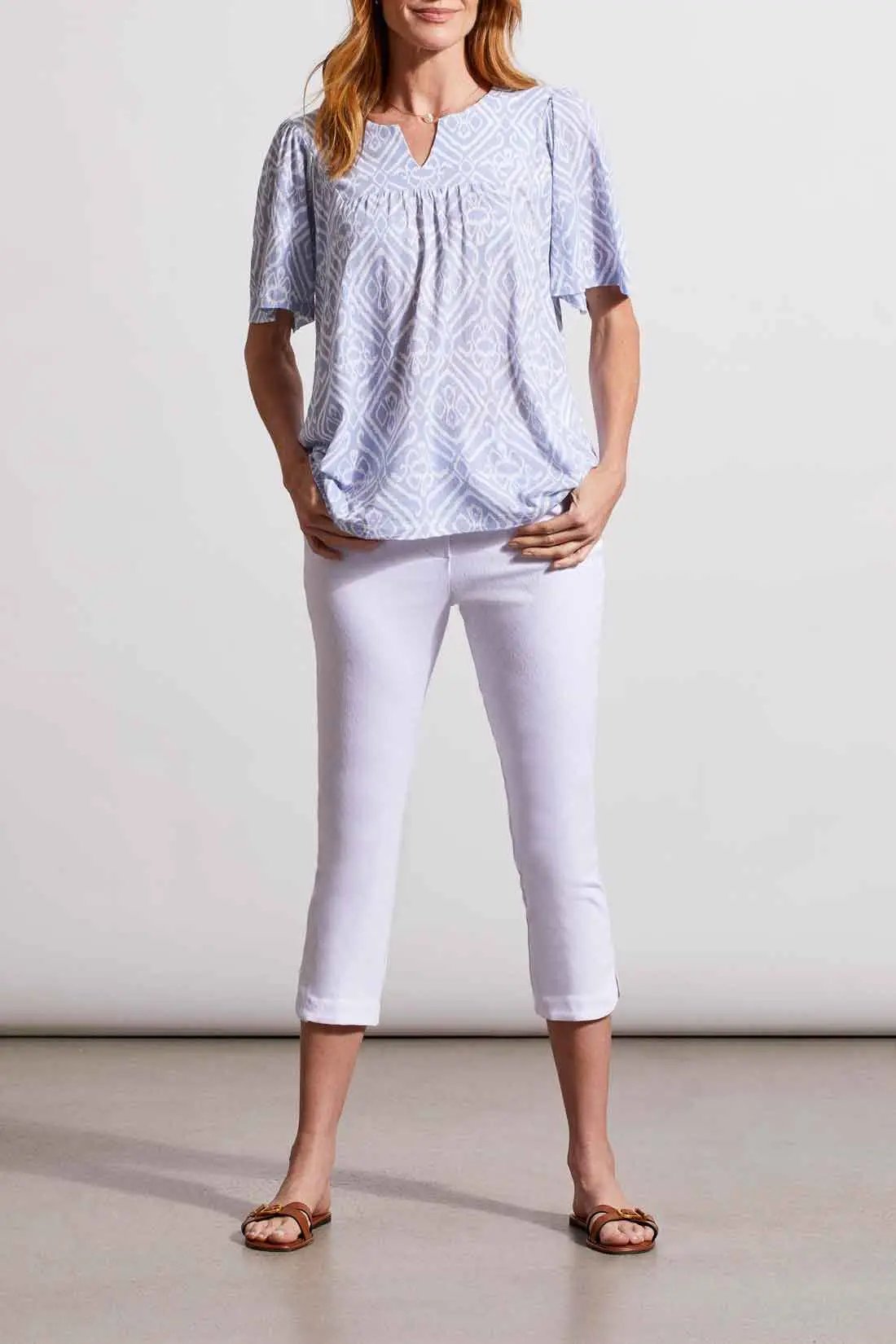 Woman standing in a Tribal printed blue elbow sleeve flare top with white cropped pants.