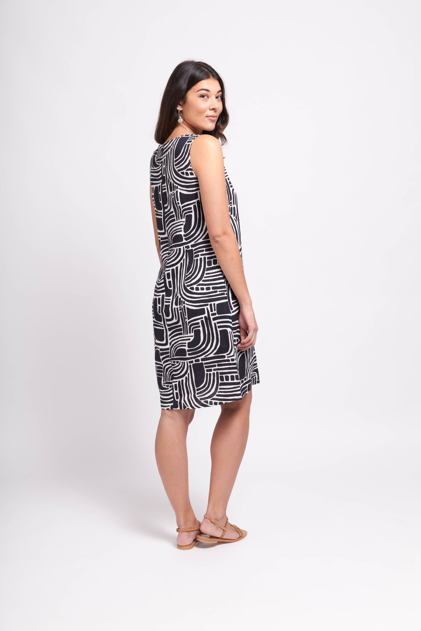 A woman in a sleeveless black and white Floral Sun Keyhole Dress with Pockets by Foil stands sideways, looking over her shoulder in a white studio setting.