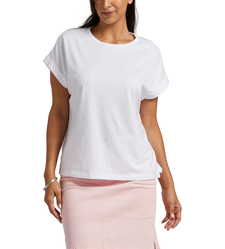 A person in a Jag Drapey Luxe Tee with rolled cap sleeves and a pink skirt, standing with one hand slightly raised and the other by their side.