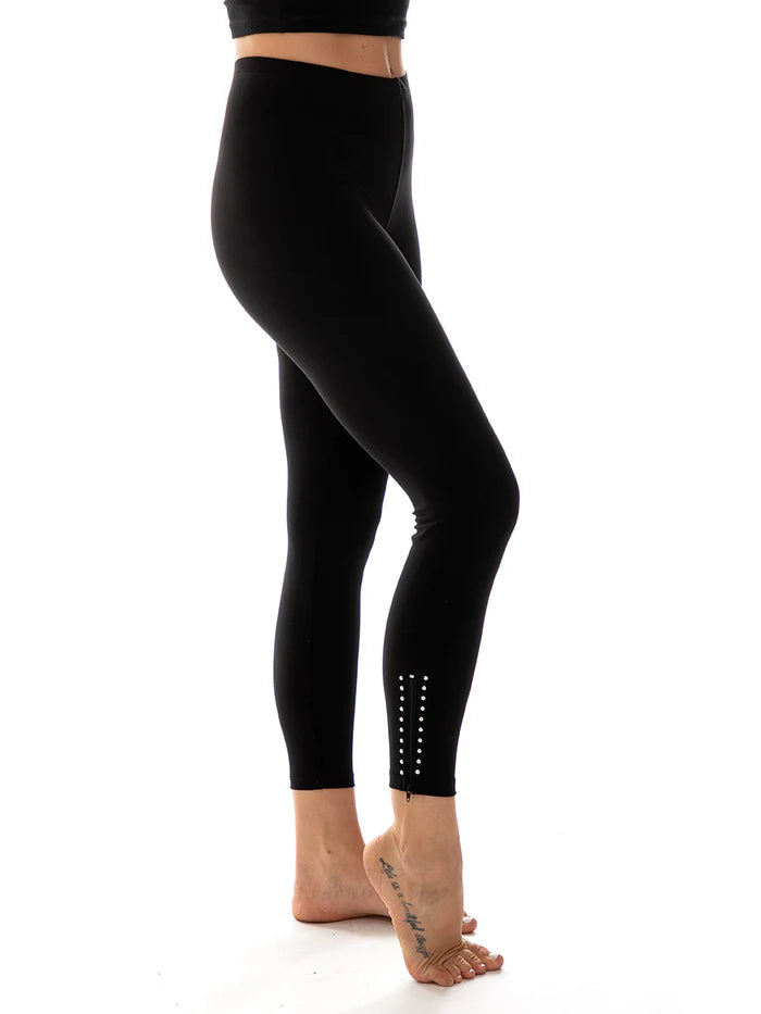 A person wearing black Bali Hamline Zip-up Leggings, standing on one foot. The leggings feature a chic silver stud detail near the ankle, adding an elegant touch to any fitness routine.