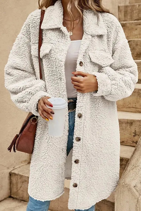 A person wearing a Plain Button Up Sherpa Jacket in White by UNISHE holds a coffee cup and a brown shoulder bag.