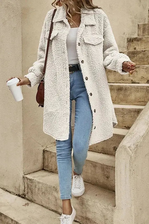 A person wearing a Plain Button Up Sherpa Jacket in White by UNISHE holds a coffee cup and a brown shoulder bag.