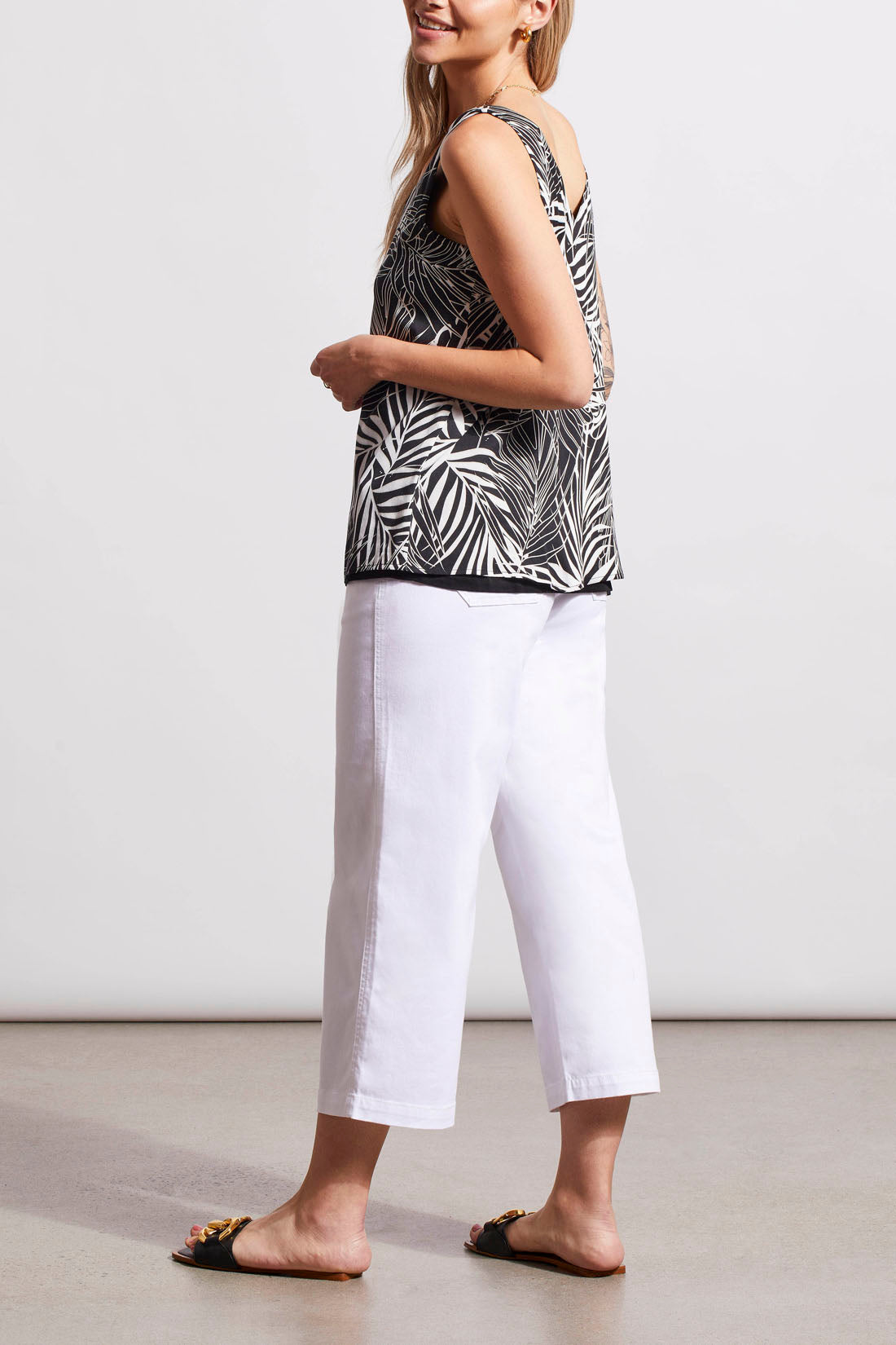 A woman wearing a Tribal reversible sleeveless V-Neck Cami top and white capri pants with slip-on sandals.