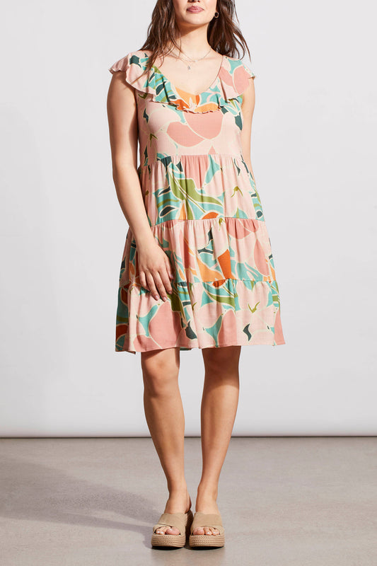 A woman in a Tribal sleeveless dress with lining, floral print and tie back, paired with beige sandals standing against a plain backdrop.