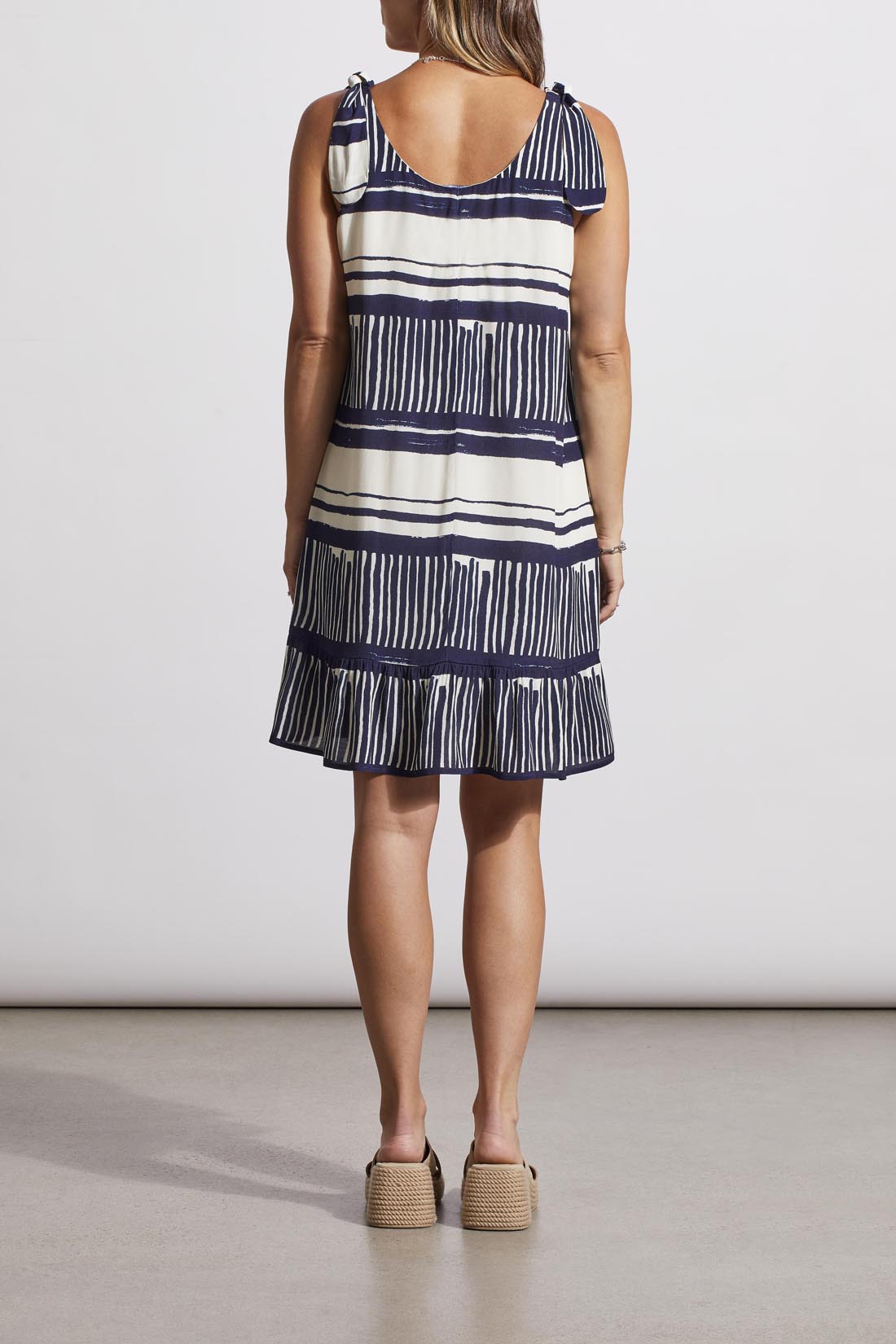 A person wearing a fashion-forward, Tribal sleeveless dress with lining and platform sandals stands against a neutral background.