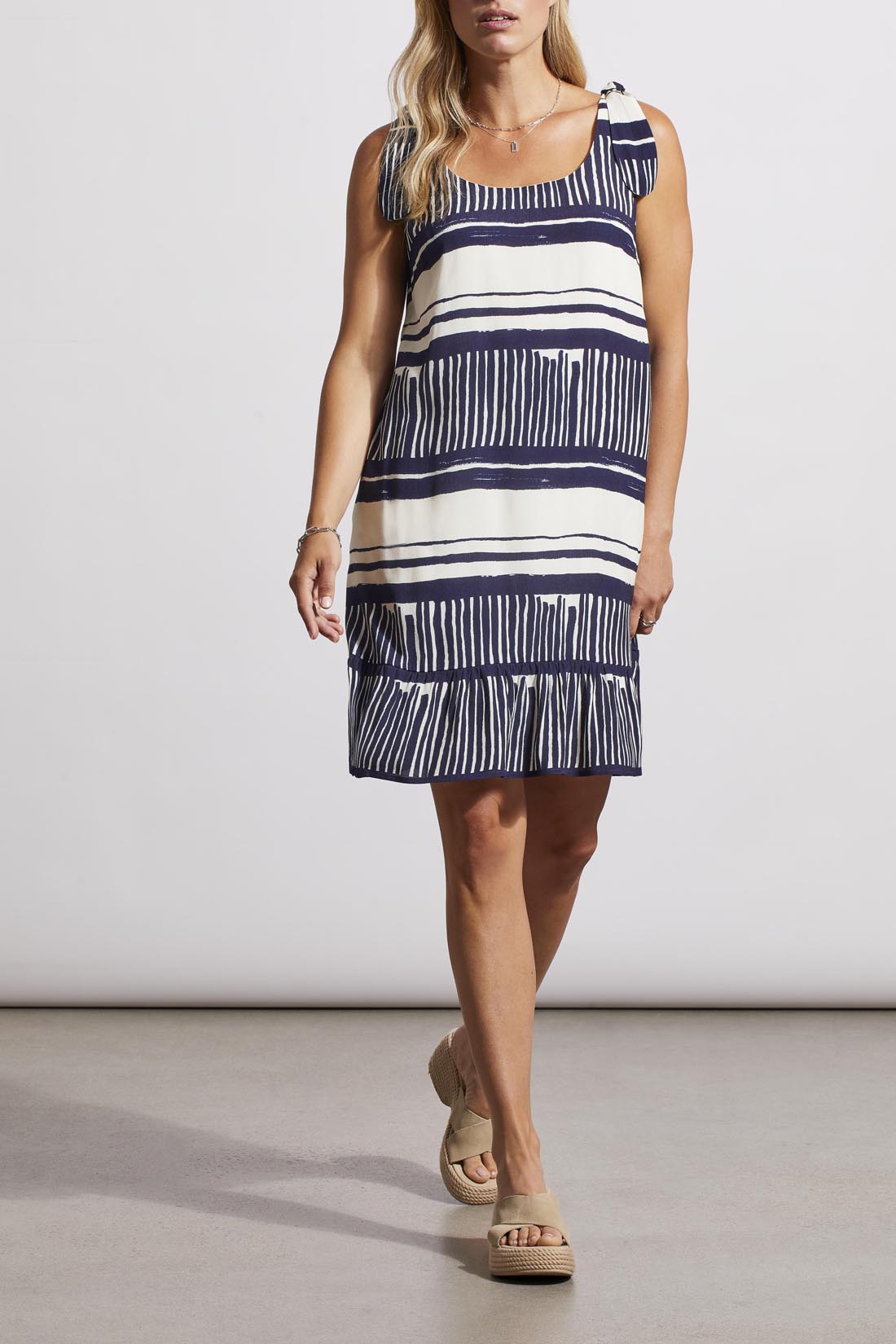 A person wearing a fashion-forward, Tribal sleeveless dress with lining and platform sandals stands against a neutral background.