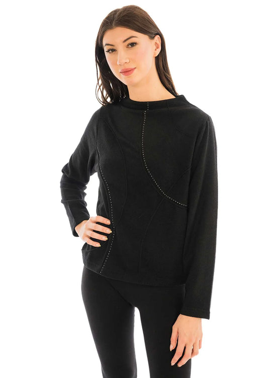 A person exudes fashion-forward elegance with one hand on their hip, wearing the sleek, long-sleeved Trisha Tyler Contrast Stitch Detail Sweater paired with matching black pants.