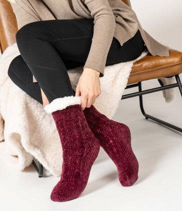 A woman sitting on a chair wearing Cray Cray Soft Slipper Socks, the slip-proof chenille fuzzy socks from Britt's Knits.