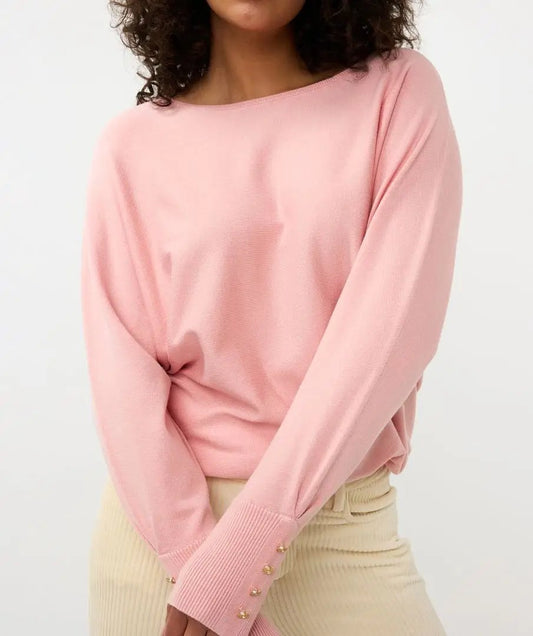 A person with curly hair is standing with their back to the camera, wearing Esqualo's pink Batwing Sweater with buttoned cuffs and light-colored pants.