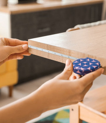 A person is using an In A Fix mini tape measure to place a piece of paper on a wooden table.