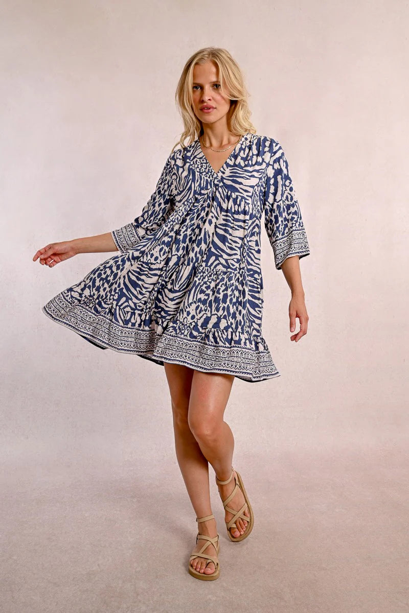 A person with long blonde hair stands against a plain backdrop, wearing the Molly Bracken 3/4 Sleeve Kimono Dress in a blue zebra print and sandals, looking to the right.