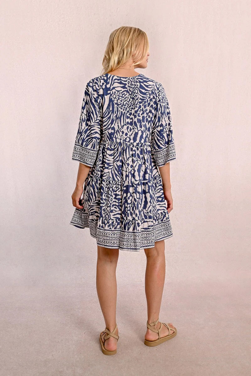 A person with long blonde hair stands against a plain backdrop, wearing the Molly Bracken 3/4 Sleeve Kimono Dress in a blue zebra print and sandals, looking to the right.