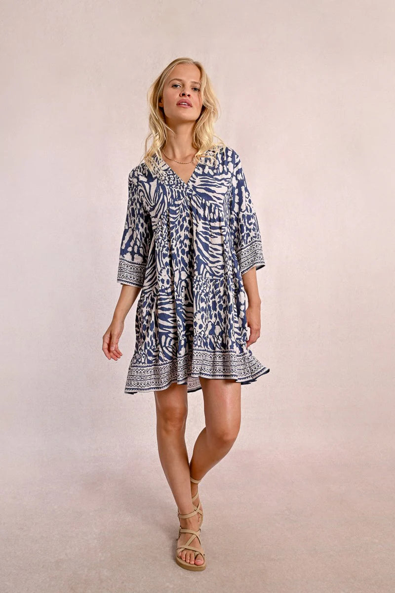 A person with long blonde hair stands against a plain backdrop, wearing the Molly Bracken 3/4 Sleeve Kimono Dress in a blue zebra print and sandals, looking to the right.