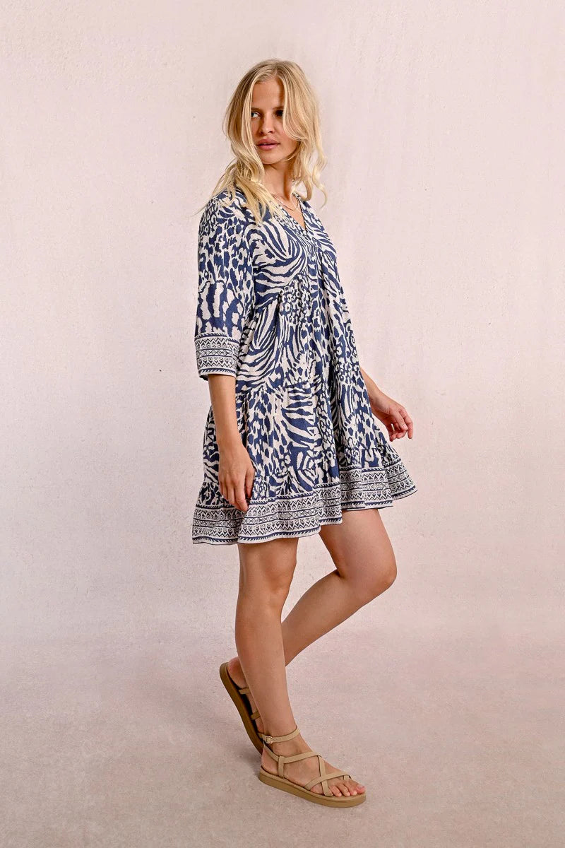 A person with long blonde hair stands against a plain backdrop, wearing the Molly Bracken 3/4 Sleeve Kimono Dress in a blue zebra print and sandals, looking to the right.