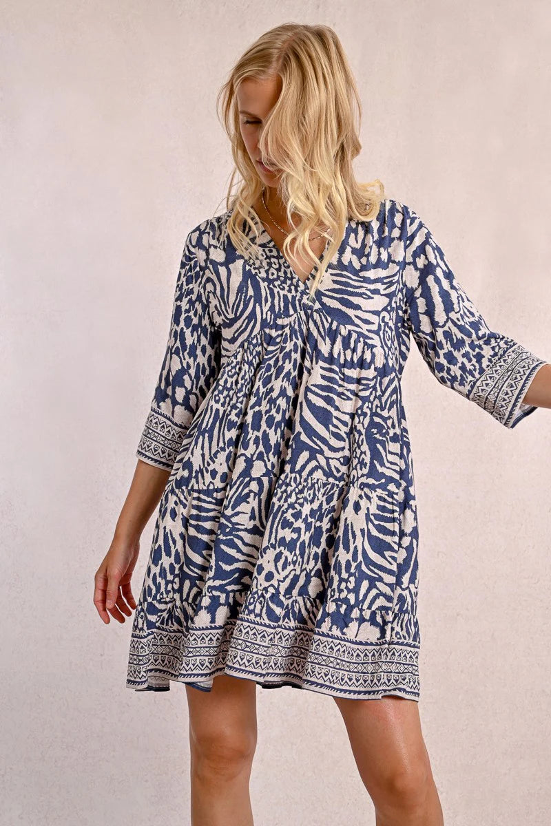 A person with long blonde hair stands against a plain backdrop, wearing the Molly Bracken 3/4 Sleeve Kimono Dress in a blue zebra print and sandals, looking to the right.