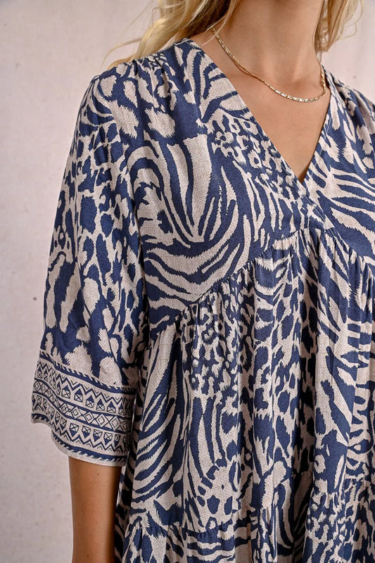 A person with long blonde hair stands against a plain backdrop, wearing the Molly Bracken 3/4 Sleeve Kimono Dress in a blue zebra print and sandals, looking to the right.