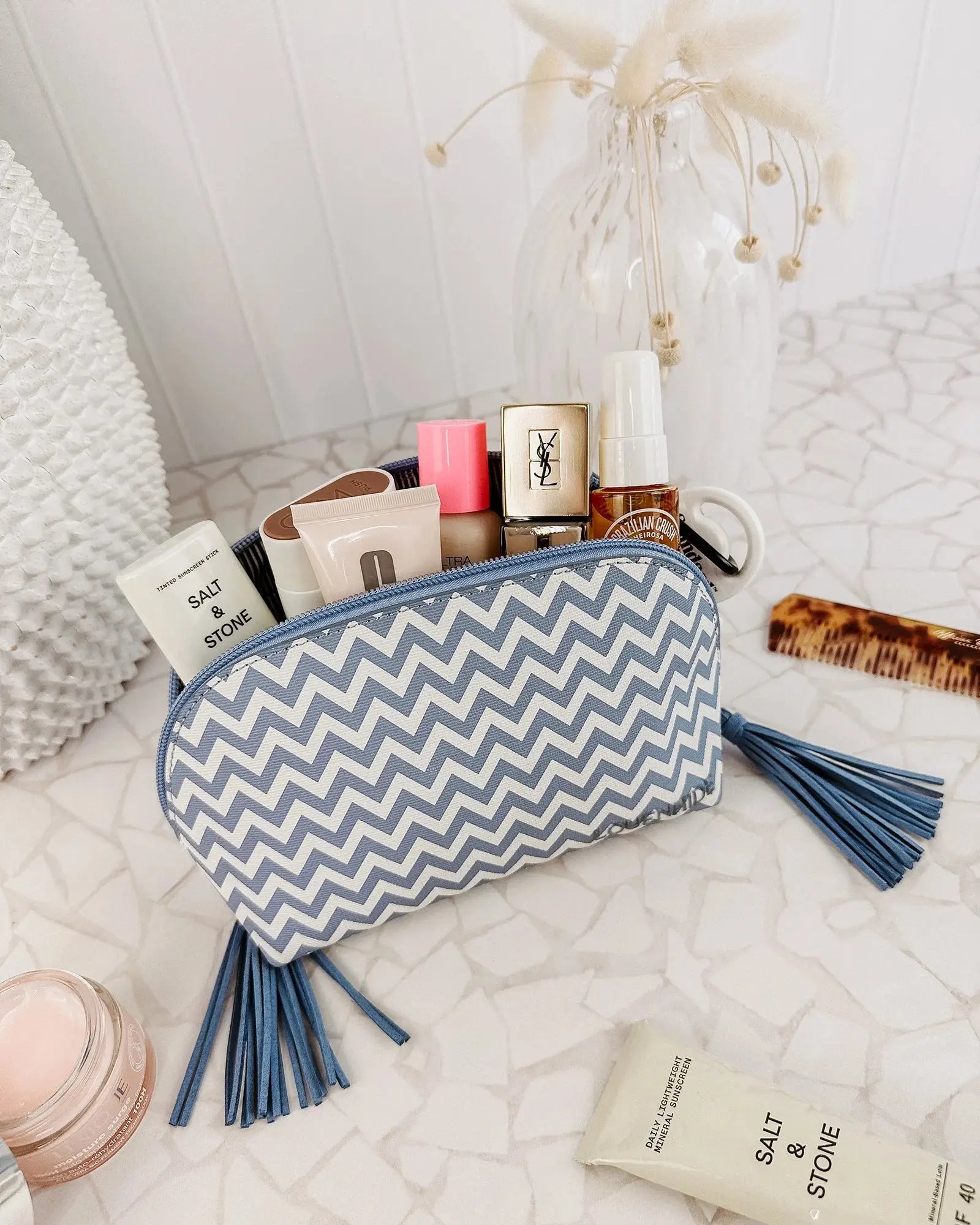 The Emma & Baby Audrey Cosmetic Set from Louenhide includes a blue rectangular travel cosmetic case with a black handle, paired with a smaller white and blue chevron-patterned pouch adorned with a pair of tassels. This set provides your largest toiletry case solution on the go.