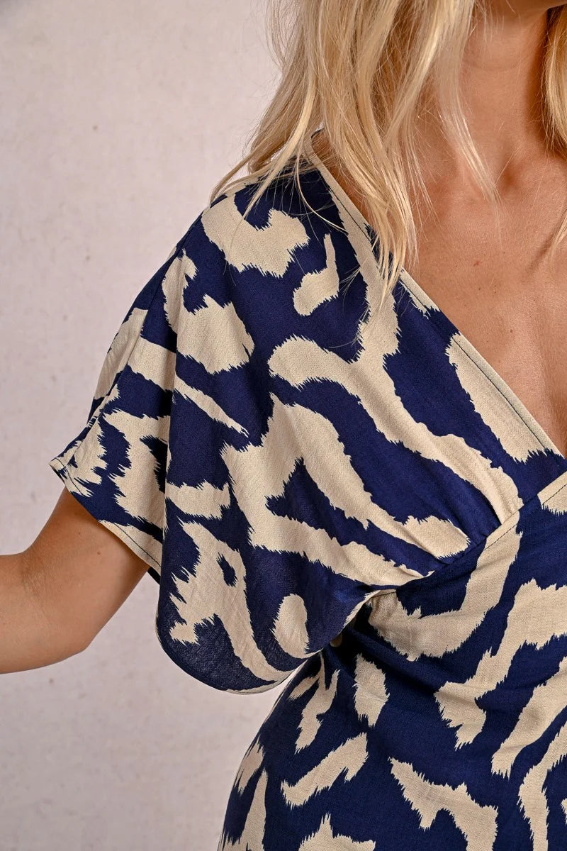 Wearing Molly Bracken's The Perfect Vacation Dress, in a blue and white pattern with lightweight fabric for a flattering silhouette, a person stands against a plain background—arms slightly out to embody the essence of this ideal vacation attire.