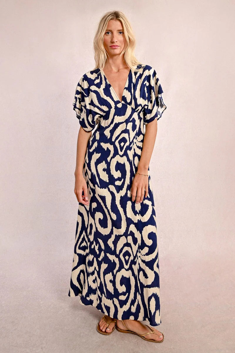 Wearing Molly Bracken's The Perfect Vacation Dress, in a blue and white pattern with lightweight fabric for a flattering silhouette, a person stands against a plain background—arms slightly out to embody the essence of this ideal vacation attire.