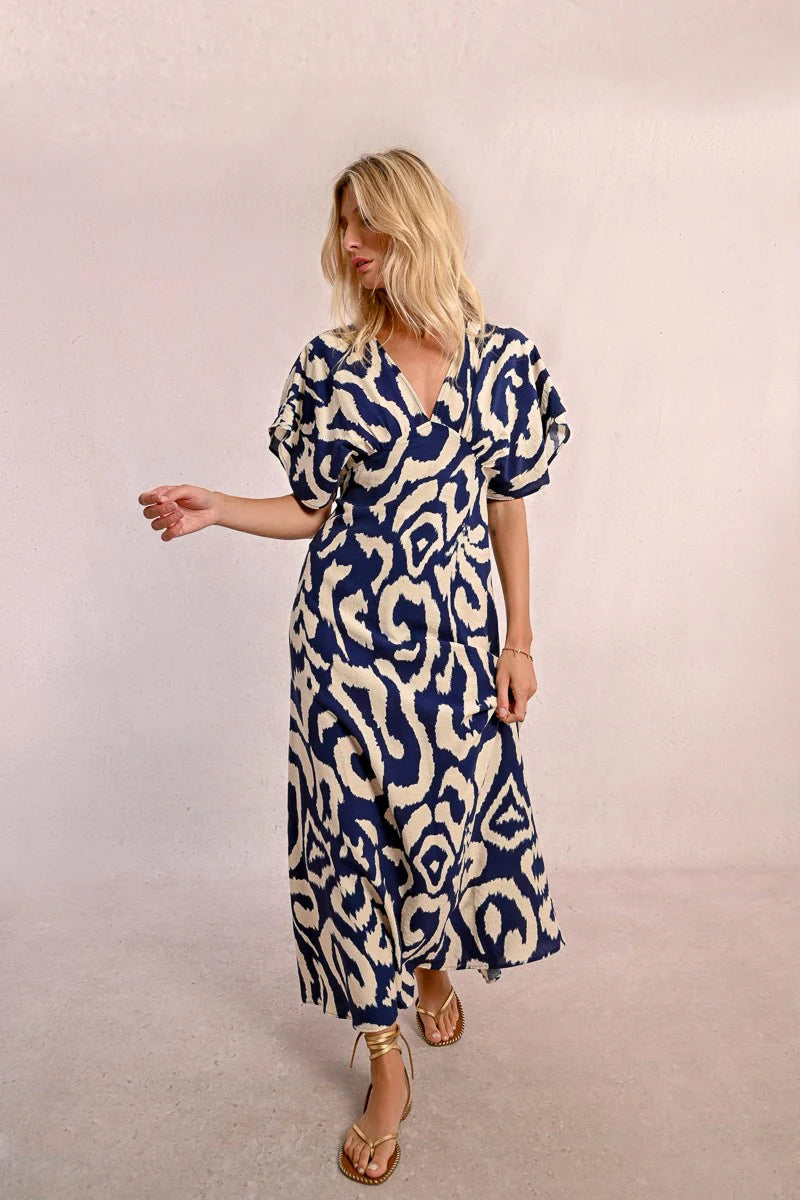 Wearing Molly Bracken's The Perfect Vacation Dress, in a blue and white pattern with lightweight fabric for a flattering silhouette, a person stands against a plain background—arms slightly out to embody the essence of this ideal vacation attire.