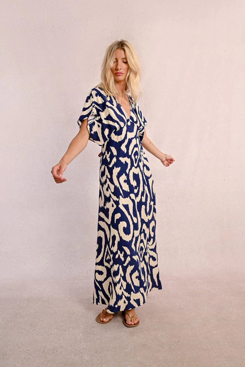 Wearing Molly Bracken's The Perfect Vacation Dress, in a blue and white pattern with lightweight fabric for a flattering silhouette, a person stands against a plain background—arms slightly out to embody the essence of this ideal vacation attire.