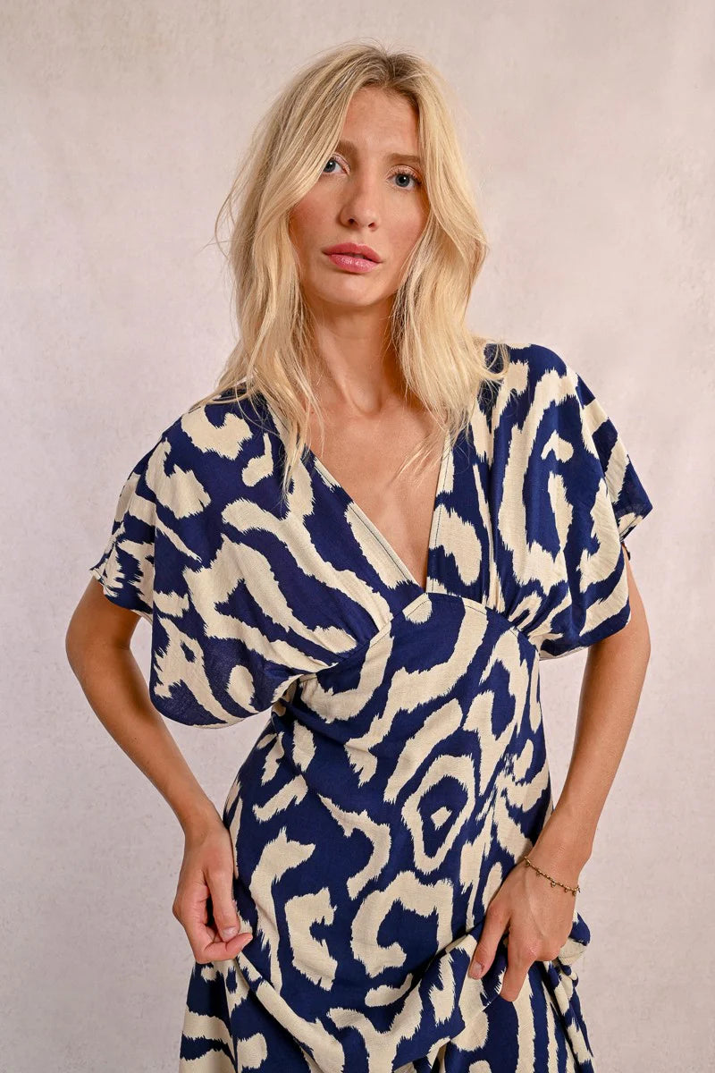 Wearing Molly Bracken's The Perfect Vacation Dress, in a blue and white pattern with lightweight fabric for a flattering silhouette, a person stands against a plain background—arms slightly out to embody the essence of this ideal vacation attire.