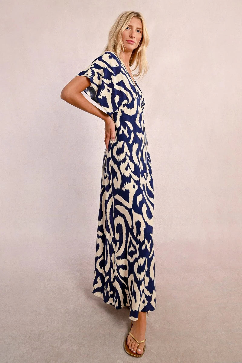 Wearing Molly Bracken's The Perfect Vacation Dress, in a blue and white pattern with lightweight fabric for a flattering silhouette, a person stands against a plain background—arms slightly out to embody the essence of this ideal vacation attire.