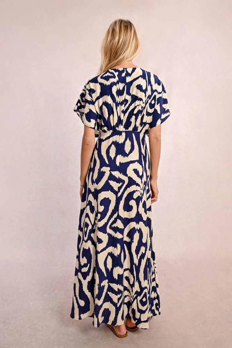 Wearing Molly Bracken's The Perfect Vacation Dress, in a blue and white pattern with lightweight fabric for a flattering silhouette, a person stands against a plain background—arms slightly out to embody the essence of this ideal vacation attire.