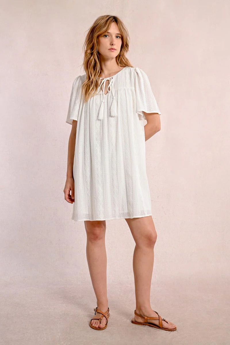 Someone in a Molly Bracken Off White Woven Dress with a v-neck and brown sandals stands against a plain background, looking to the side.