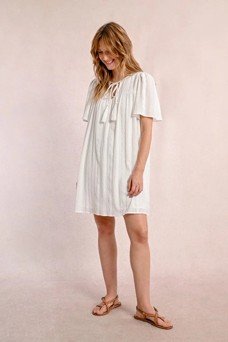 Someone in a Molly Bracken Off White Woven Dress with a v-neck and brown sandals stands against a plain background, looking to the side.