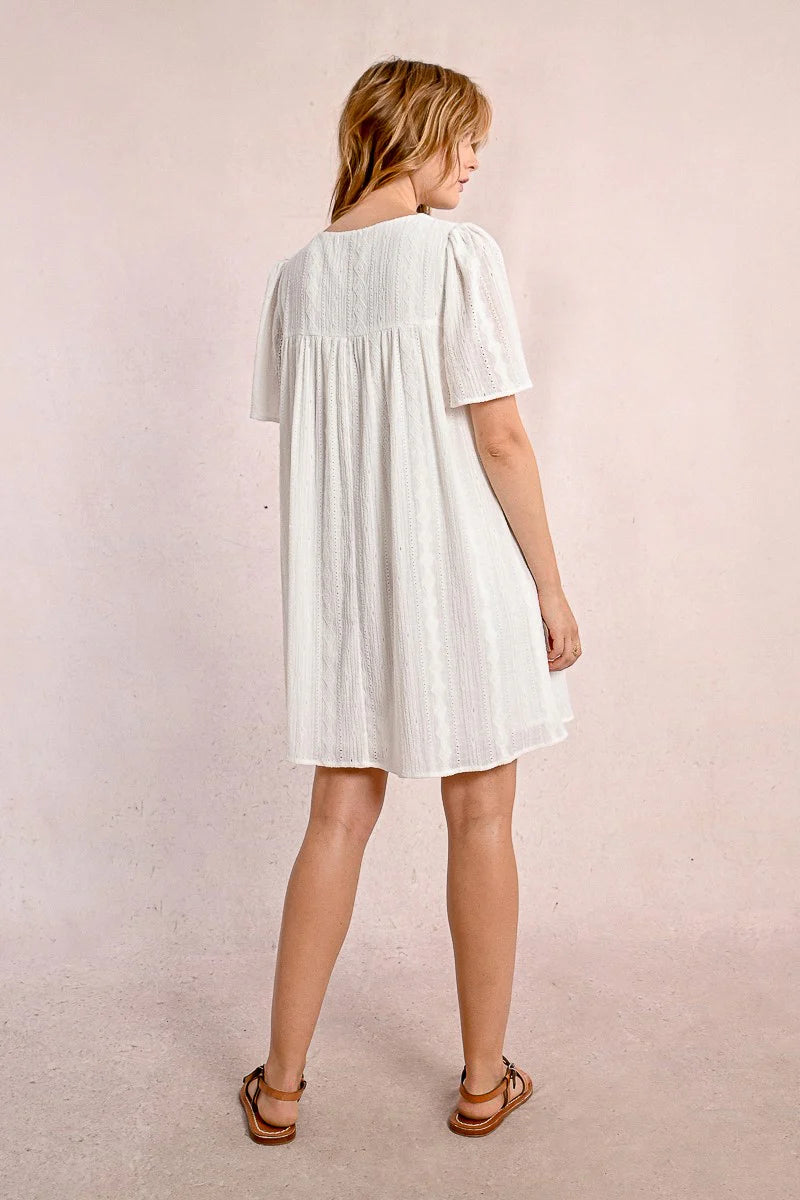 Someone in a Molly Bracken Off White Woven Dress with a v-neck and brown sandals stands against a plain background, looking to the side.