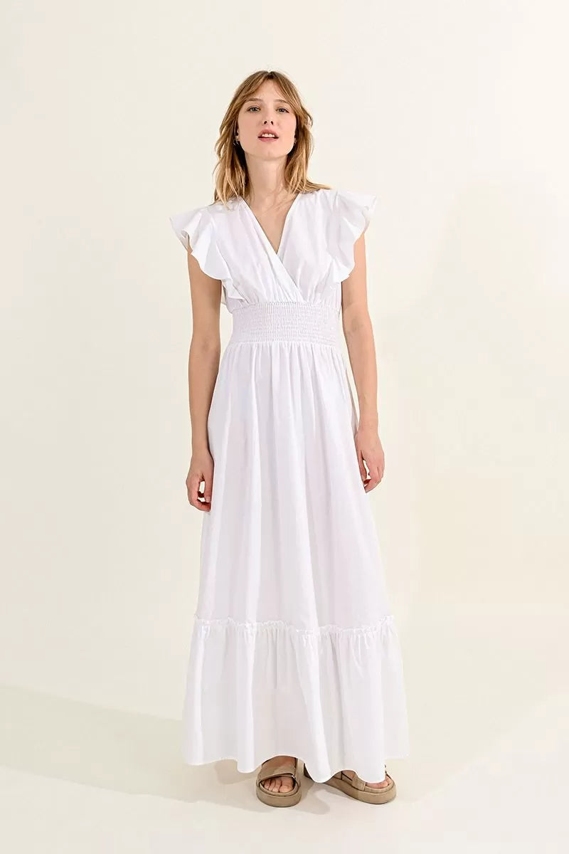 A woman in a white Molly Bracken ruffled V-neck maxi dress with a smocked waist standing against a neutral background.