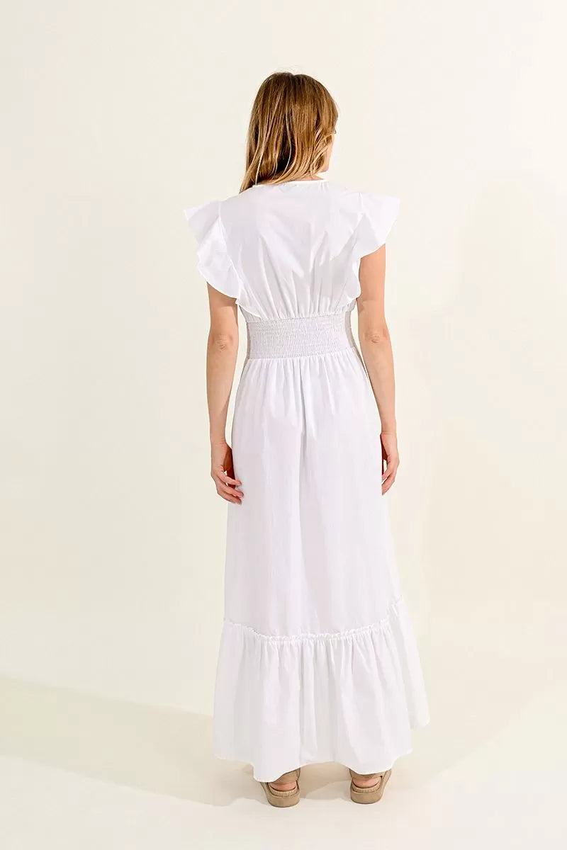 A woman in a white Molly Bracken ruffled V-neck maxi dress with a smocked waist standing against a neutral background.