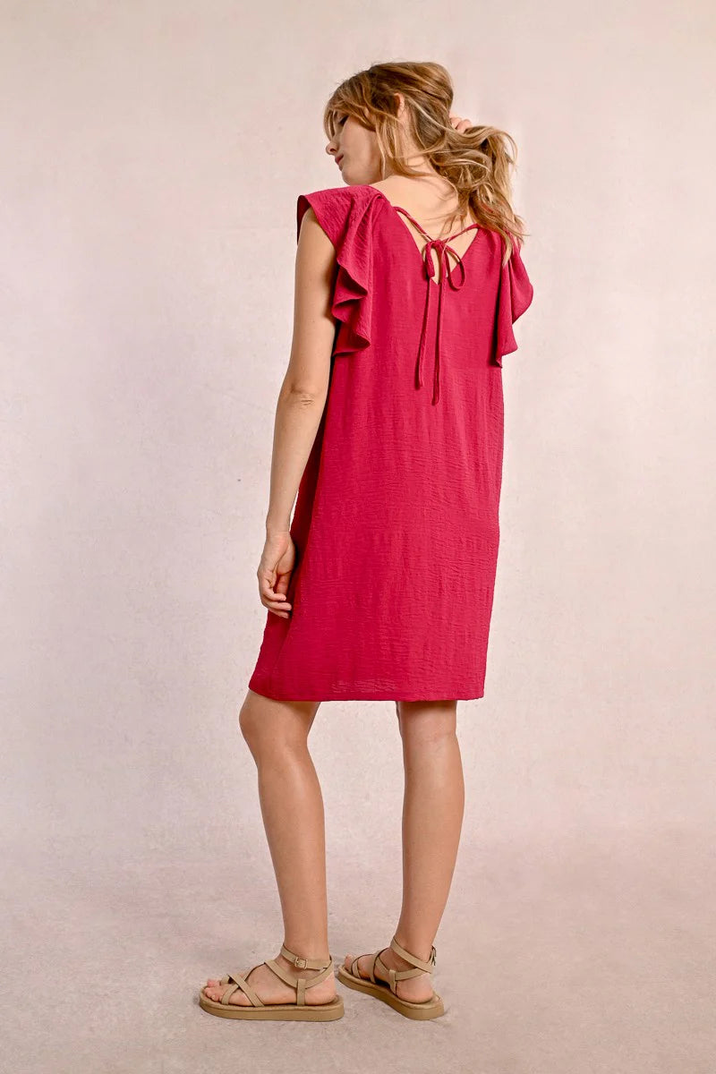 Against a neutral background, someone wears Molly Bracken's knee-length Round Neck Back Tie Short Dress with ruffled sleeves in red, paired with beige sandals.