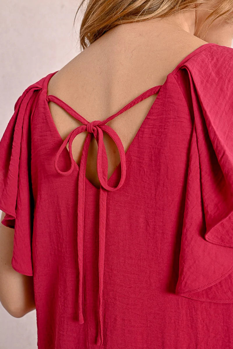 Against a neutral background, someone wears Molly Bracken's knee-length Round Neck Back Tie Short Dress with ruffled sleeves in red, paired with beige sandals.