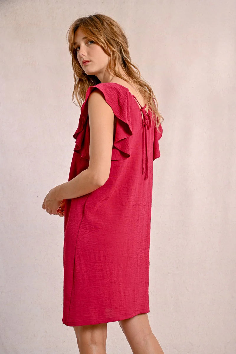 Against a neutral background, someone wears Molly Bracken's knee-length Round Neck Back Tie Short Dress with ruffled sleeves in red, paired with beige sandals.