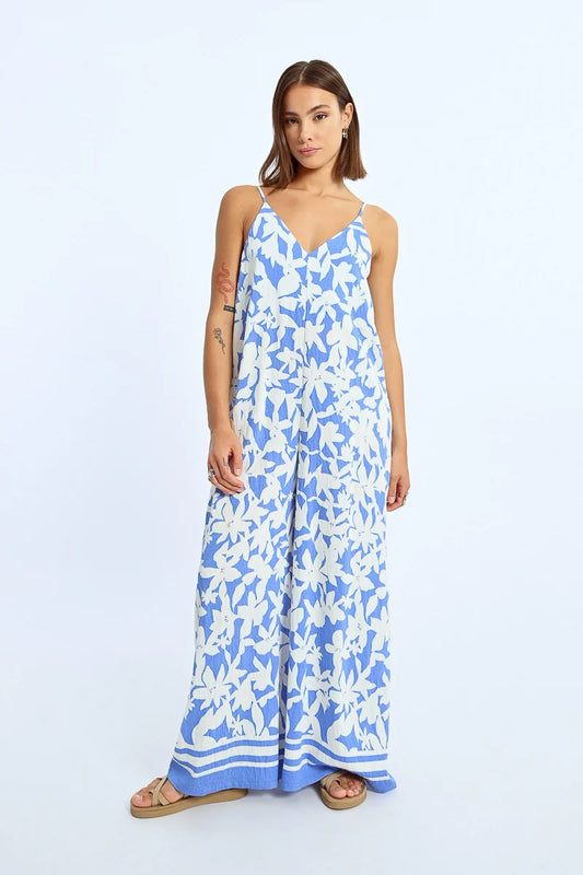 A woman exudes effortless style in a Molly Bracken Wide Leg Strappy Jumpsuit, paired with sandals, against a plain background.