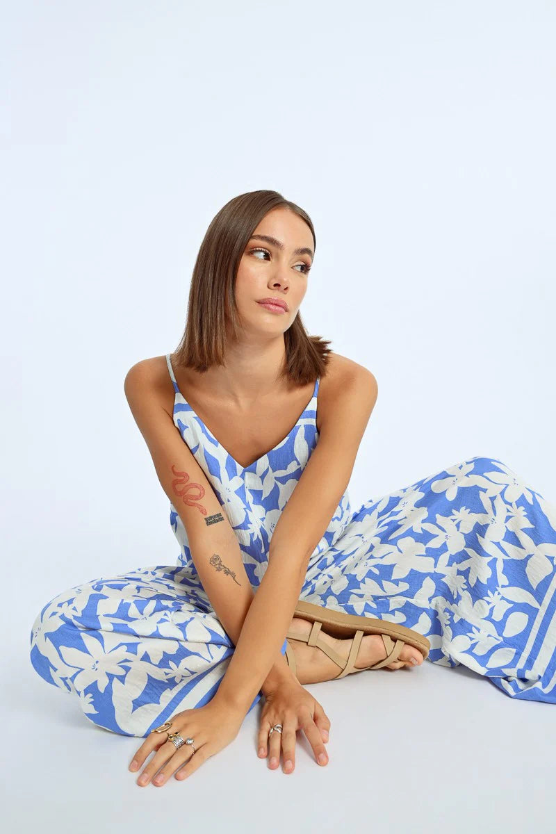 A woman exudes effortless style in a Molly Bracken Wide Leg Strappy Jumpsuit, paired with sandals, against a plain background.