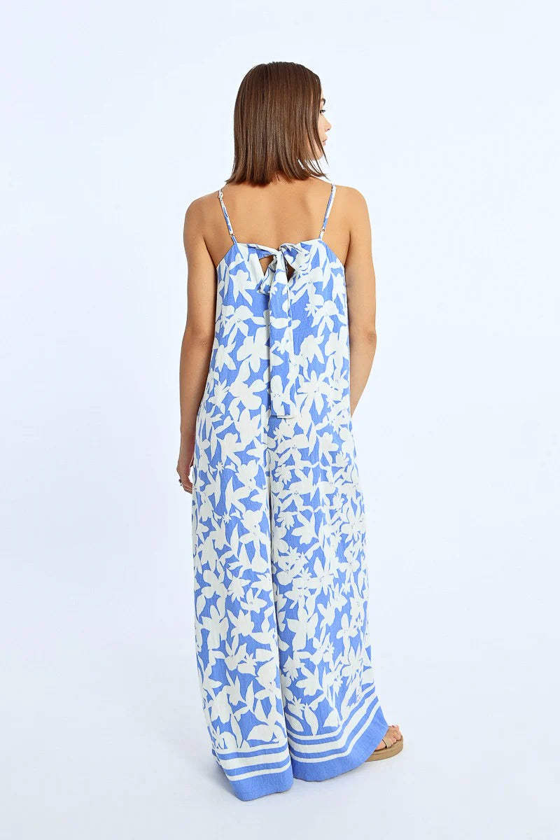 A woman exudes effortless style in a Molly Bracken Wide Leg Strappy Jumpsuit, paired with sandals, against a plain background.