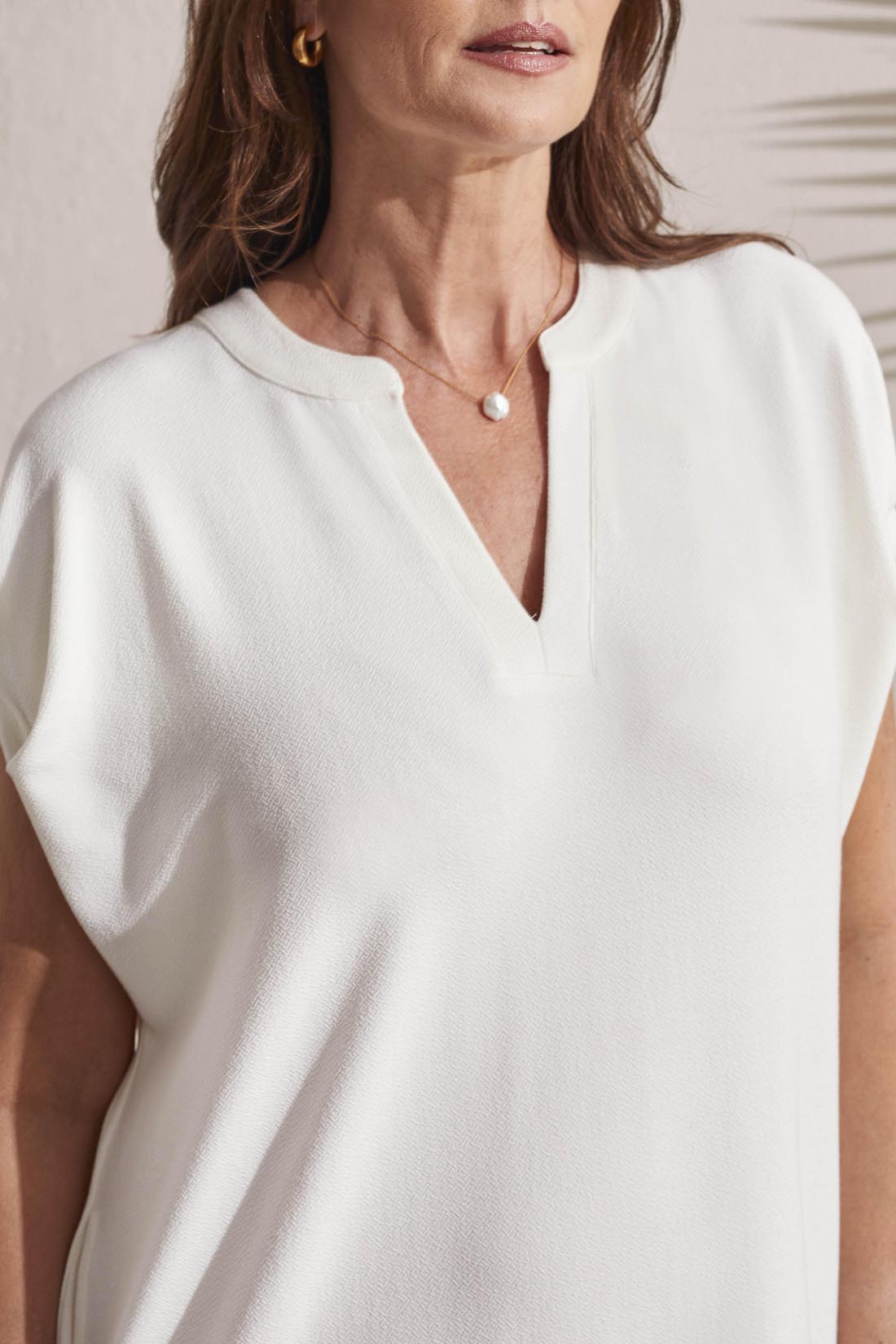 Woman in a versatile white Tribal Shift Knit Dress with a V-neckline and short sleeves, adorned with a pearl necklace.
