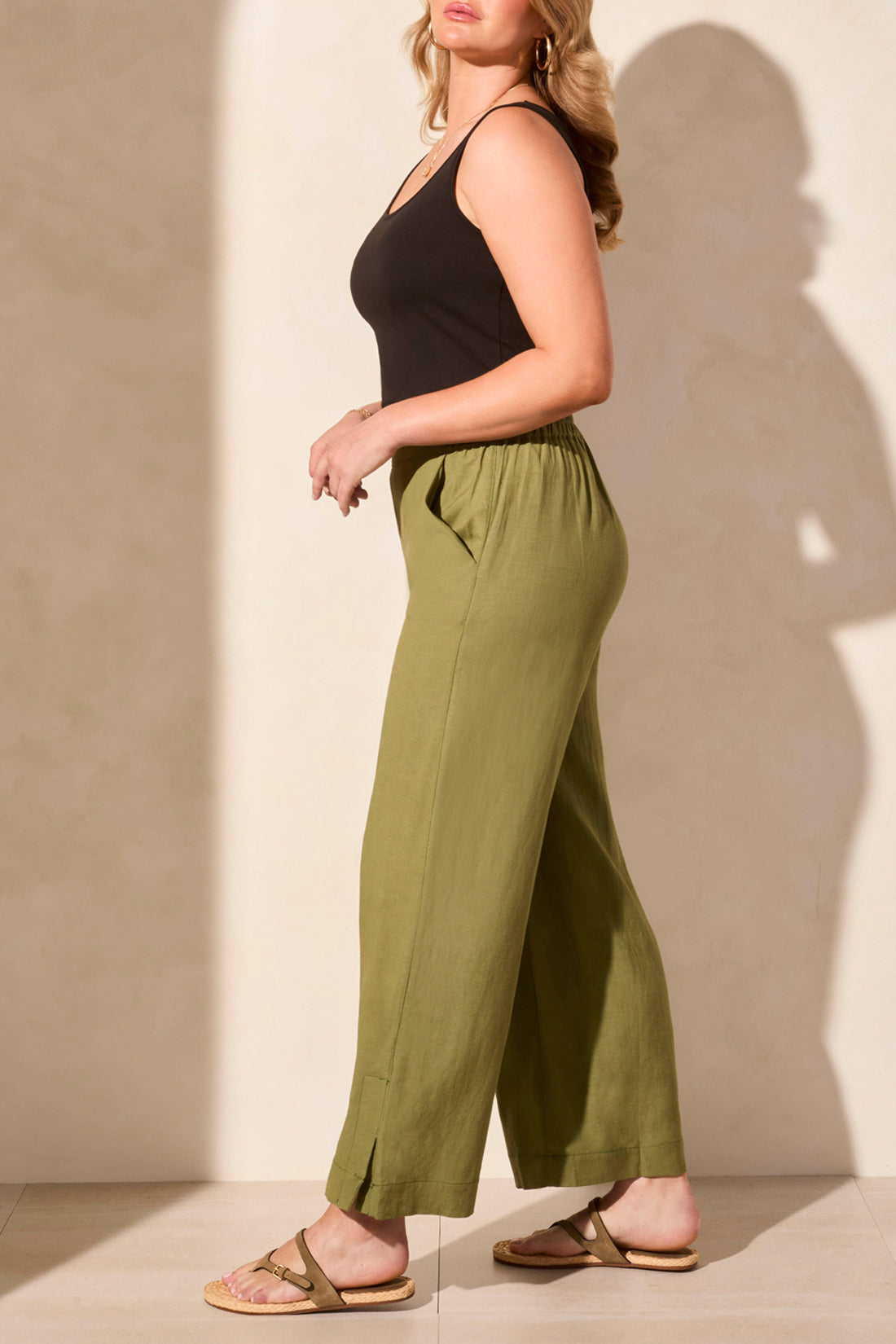 A woman in a sleeveless red top and Tribal's PULL ON ANKLE PANT W/ HEM VENT stands against a light background. Her look is super cute, completed by comfy open-toed sandals.